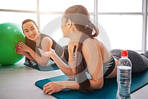 Two young cheerful woman exercising in fitness room. Asian model look ar her friend. They talk and lay on matrass. Young