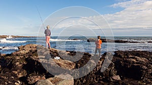 Two young children fishing off the rocks into the sea photo