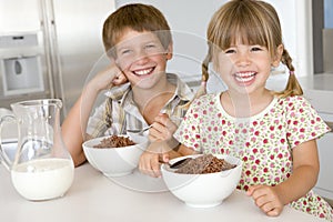 Two young children in kitchen eating cereal