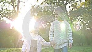 Two young children, an older boy and a younger girl, are walking in the park, holding hands. The children are in high