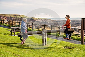 Two young children playing on a seesaw in a park by the sea