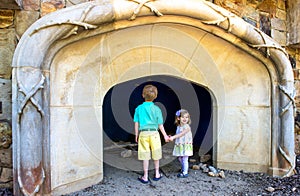 Two young children regard a cave opening at a public garden