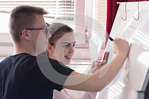 Two young college students writing on the chalkboard/blackboard during a  class. Resolving math problem or presenting their idea