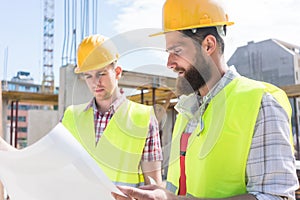 Two young construction workers analyzing together the plan of a
