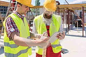 Two young construction workers smiling while using a tablet duri