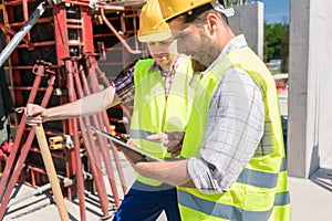 Two young construction workers smiling while using a tablet duri