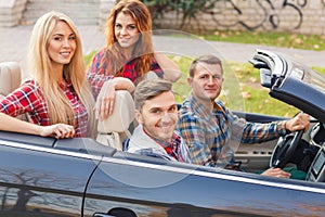 Two young couples ride in a black convertible