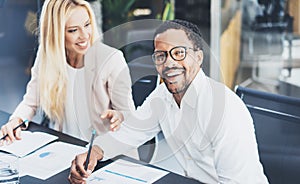 Two young coworkers working together in a modern office.Man wearing glasses, looking at the camera and smiling.Woman discussing wi