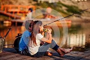 Two young cute little friends, boy and girl eating sandwiches and fishing on a lake in a sunny summer day