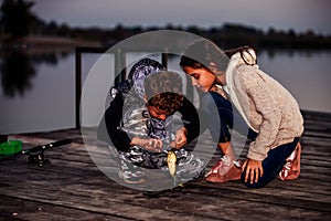 Two young cute little friends, boy and girl fishing on a lake in the evening