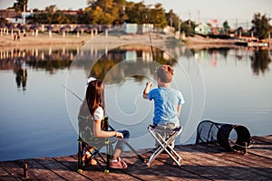 Two young cute little friends, boy and girl fishing on a lake in a sunny summer day