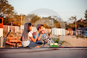 Two young cute little friends, boy and girl talking, drinking tea, eating sandwiches and fishing on a lake in a sunny summer day