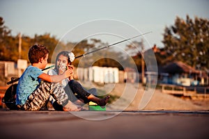 Two young cute little friends, boy and girl talking, eating sandwiches and fishing on a lake in a sunny summer day