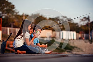 Two young cute little friends, boy and girl talking, eating sandwiches and fishing on a lake in a sunny summer day