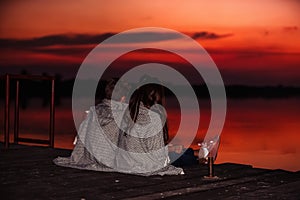 Two young cute little friends, boy and girl talking while sitting covered with blanket during sunset