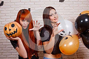 Two young cute women with pumpkin and painted balloons frighten