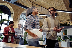 Two young diverse business people, male and female coworkers talking about something while walking in the modern office photo