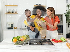 Two young diverse lesbian women spending time in a kitchen at home, harmoniously sharing food preparation duties whilst