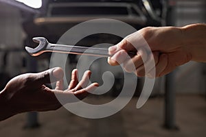 Two diverse mechanics hands giving, sharing tool to each other