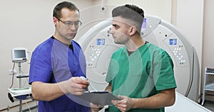 Two young doctors discussing the history of the patient on a background of a new magnetic resonance imaging.