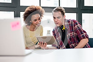 Two young employees watching a video on tablet PC in the office