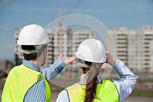 Two Young Engineers A Man And A Woman In Green Vests And Helmets