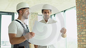 Two young engineers in safety helmets with a design plan standing on the construction site. Building bussiness. The