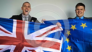 Two young English and European fans in their jackets are holding the English and the European flag in their hands arguing rejoici