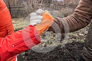 Two young farmers shake hands on the background of the soil in the spring, the farmer`s agreement. The concept of teamwork in