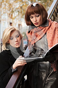 Two young fashion business women with a folder on city street