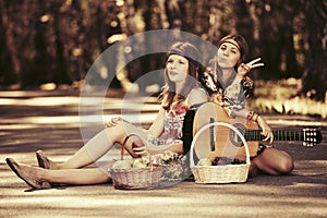 Two young fashion girls with fruit baskets sitting on the road