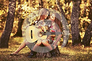 Two young fashion girls with guitar in summer forest