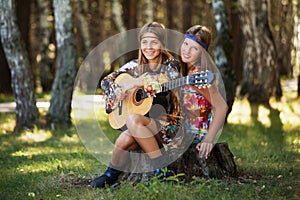 Two young fashion girls with guitar in a summer forest