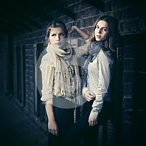 Two young fashion girls next to brick wall