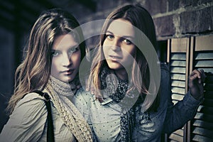 Two young fashion girls next to brick wall