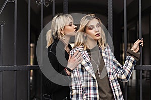 Two young fashion lesbians in stylish clothes posing in street. Sexy girl fashion model in black blazer hugs girlfriend in