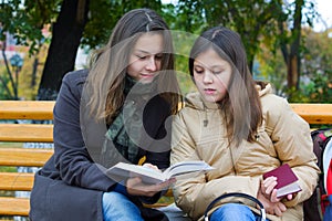 Two young fashion teen girls reading a book in park