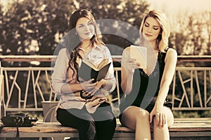 Two young fashion women with a book and digital tablet computer outdoor