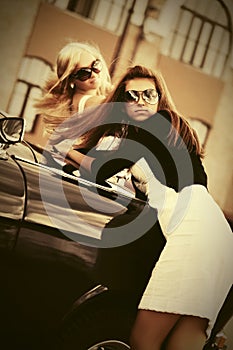 Two young fashion women leaning on vintage car
