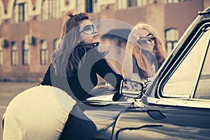 Two young fashion women leaning on vintage car on city street