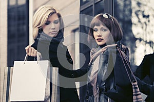 Two young fashion women with shopping bags next to mall door
