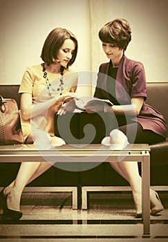 Two young fashion women sitting on couch in showroom