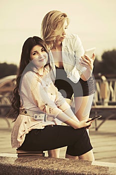 Two young fashion women using digital tablet computers outdoor