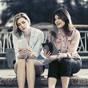 Two young fashion women using digital tablet computers outdoor