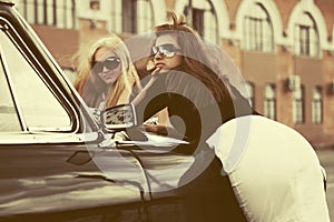 Two young fashion women by vintage car in city street