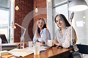 Two young female entrepreneurs sitting at work desk during the business meeting in modern conference room