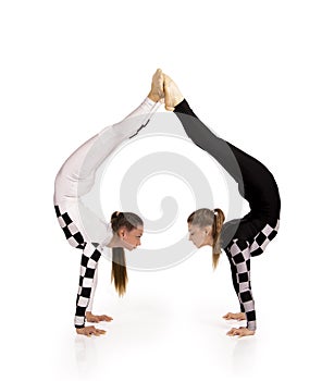 Two young female equilibrists perform acrobatic elements on a white background