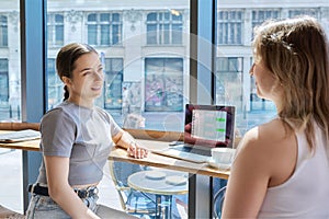 Two young female friends in cafe using laptop to chat with friends