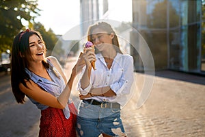 Two young female friends having fun and eating ice cream. Cheerful caucasian women eating icecream outdoors in the city