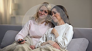 Two young female friends watching soap opera at home and crying, happy end